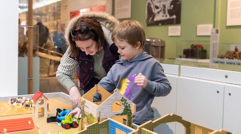 Family playing at the farm table in the Toys gallery at The MERL