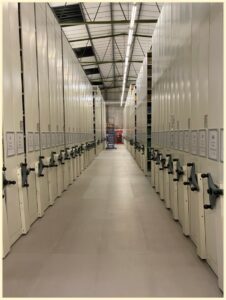 An image showing numerous rows of roller racking disappearing into the distance. A blue ladder at the far end is dwarfed by the height of the racks.